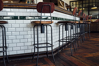 Retro wooden bar stools lined up against white subway tiles