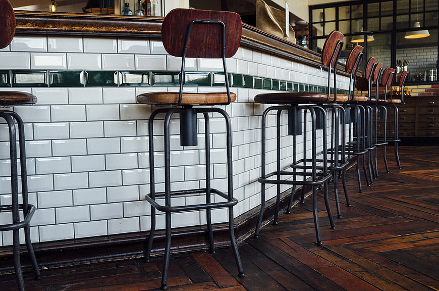 Retro wooden bar stools lined up against white subway tiles