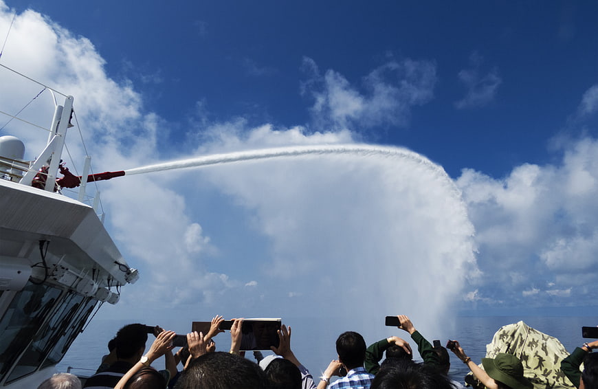 Water cannon spray from ship deck with crowd filming