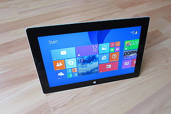 Microsoft Surface Tablet Displaying Windows 8 Start Screen on Wooden Surface