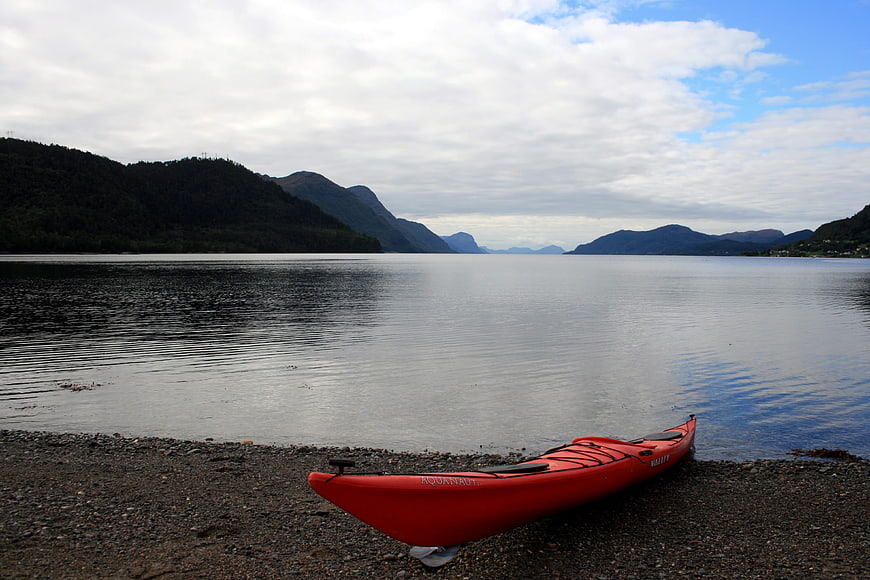 Red Kayak on Pebble Beach with Mountain Fjord View
