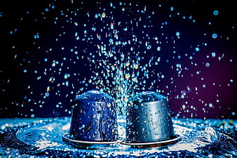 Two coffee capsules splashing in water with blue lighting