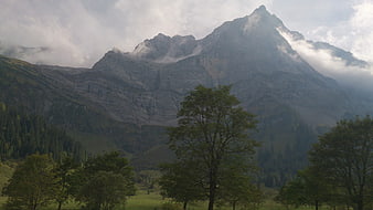 Majestic mountain peak with clouds and green trees