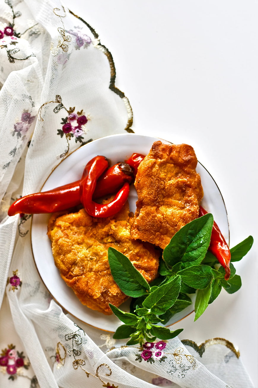 Fried fish fillets with red peppers and fresh herbs on white plate