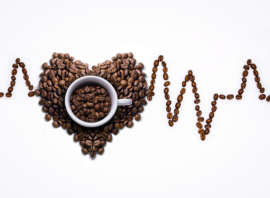Coffee beans arranged in heart and heartbeat line on white background