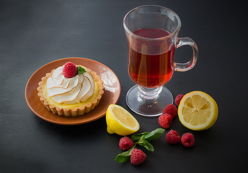 Lemon meringue tart with raspberry and glass of tea on dark surface