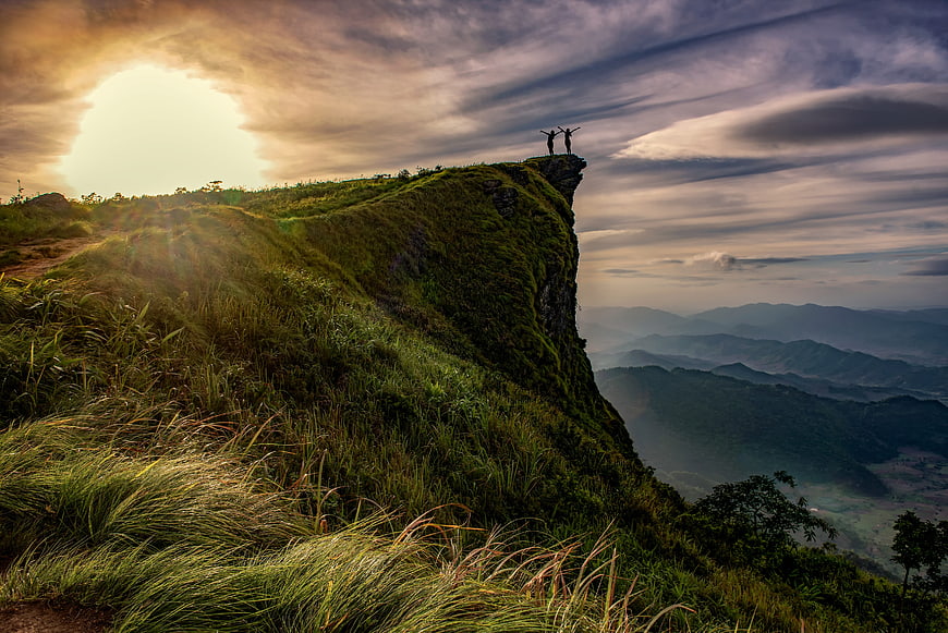 Hikers celebrating on grassy cliff edge at sunrise