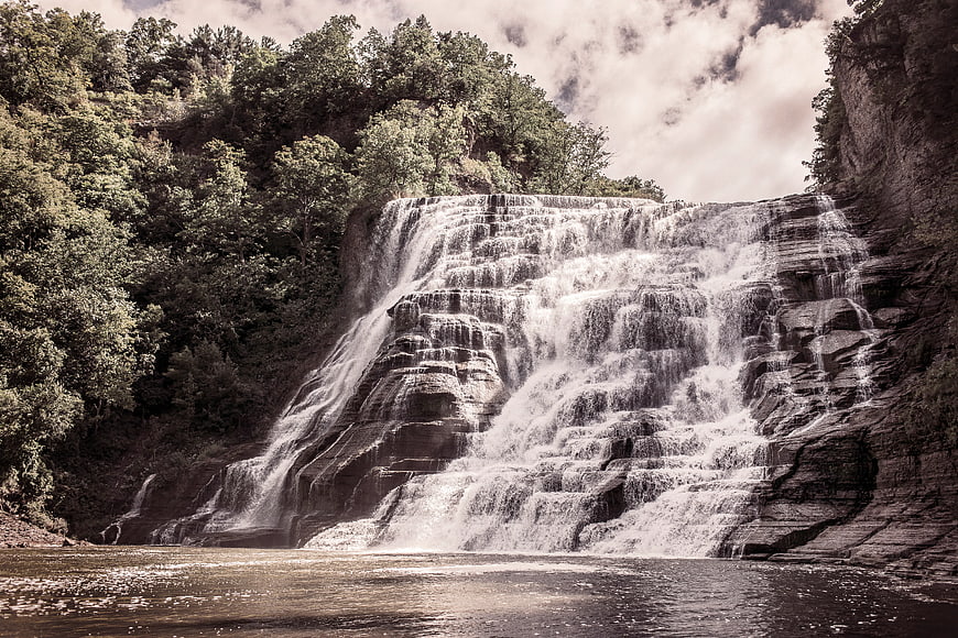 Wide cascading waterfall flowing over layered rocks in forest