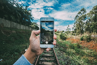 Hand holding smartphone photographing train tracks in nature