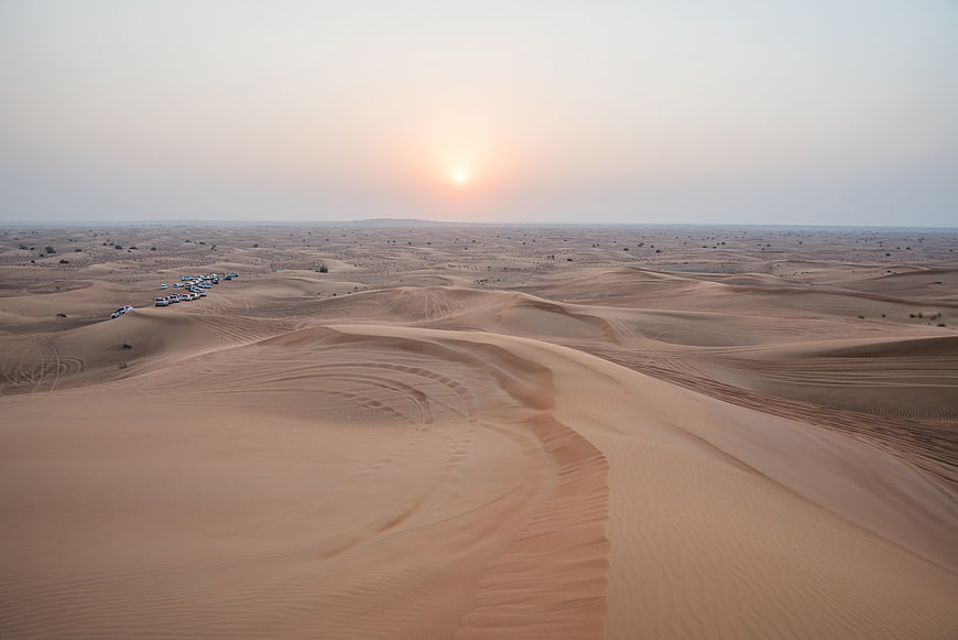 Aerial View of Desert Dunes and Vehicle Convoy at Sunset