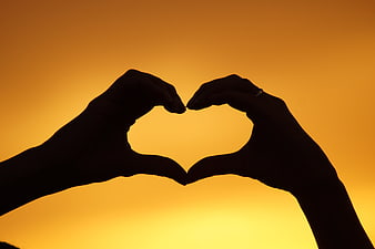 Silhouette of hands forming a heart shape against a warm sunset sky