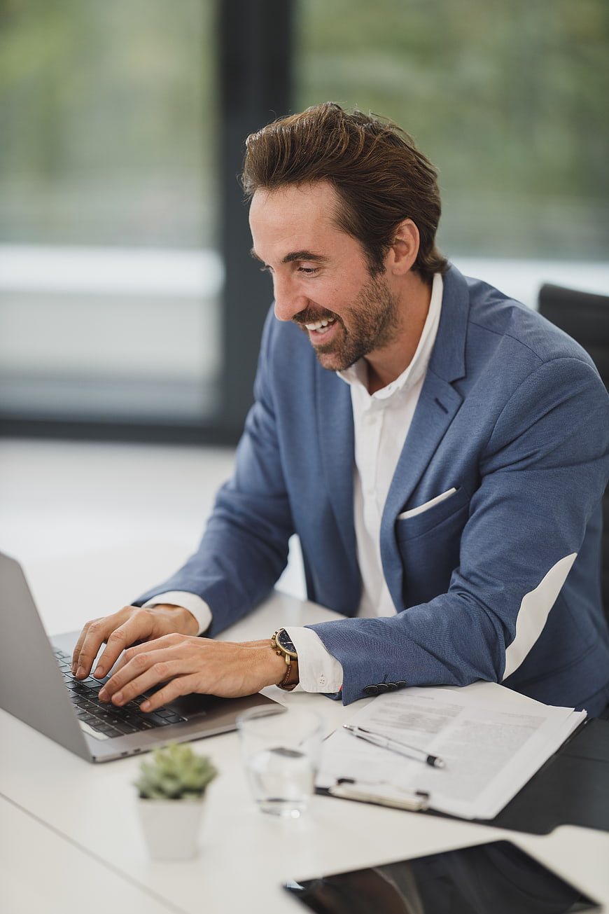 Happy businessman typing on laptop in modern office