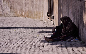 Man Sitting Alone on Cobblestone Street in Shadow