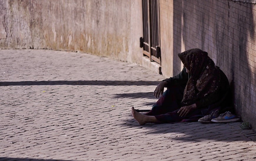Man Sitting Alone on Cobblestone Street in Shadow