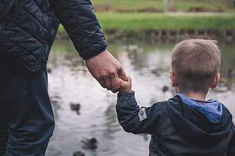 Father and son holding hands watching ducks in park pond
