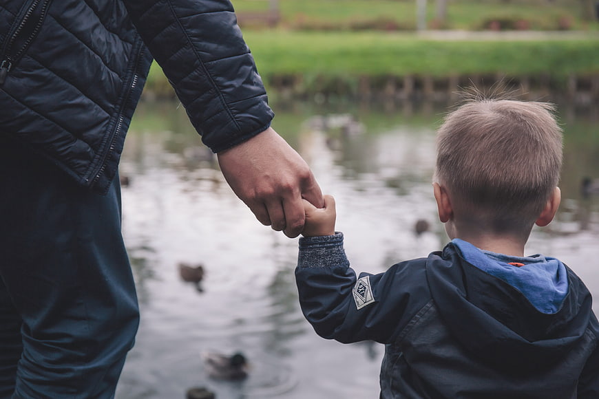 Father and son holding hands watching ducks in park pond