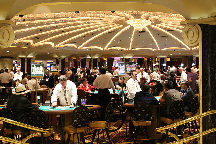 Busy Casino Floor with Dealers and Players Under Chandelier