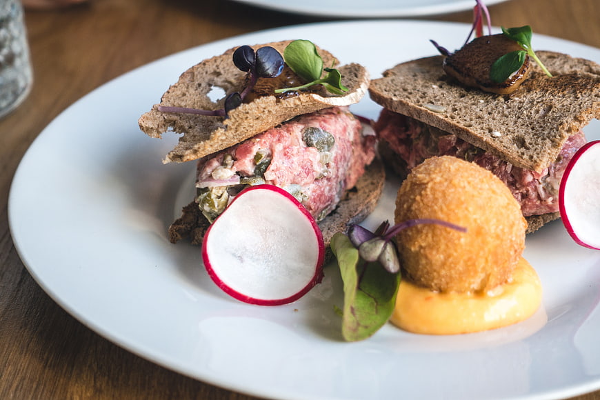 Gourmet steak tartare with radish and croquette on white plate