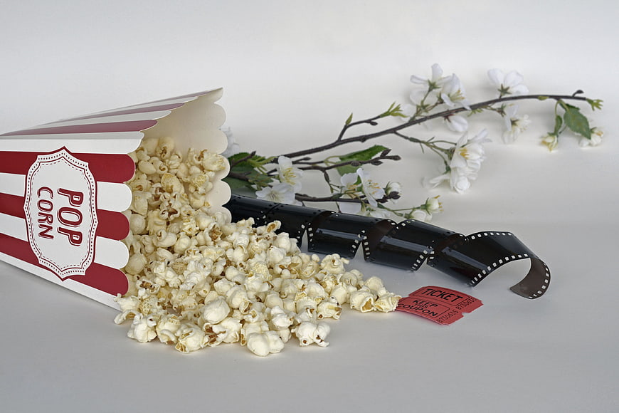 Popcorn box, film strip, and ticket with white flowers on white background