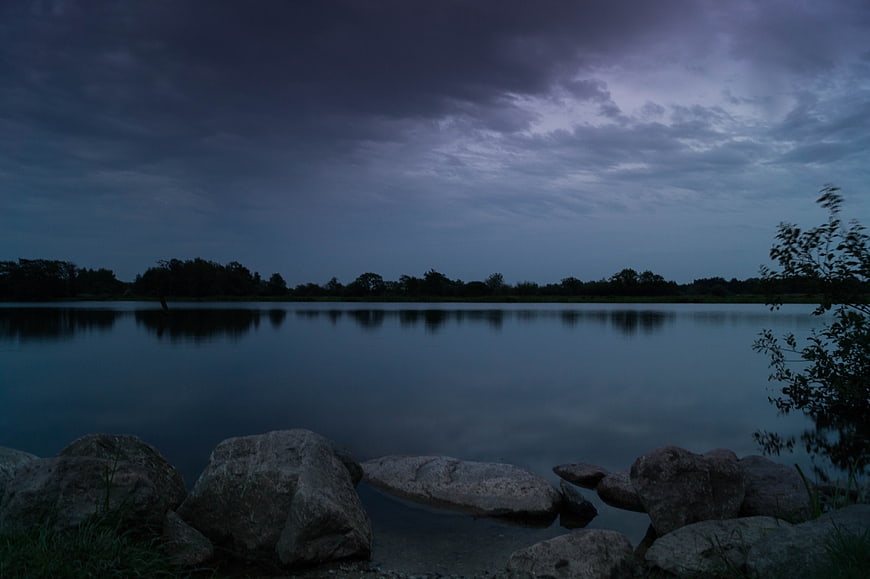 Tranquil Lake at Dusk with Rocky Shore and Cloudy Sky