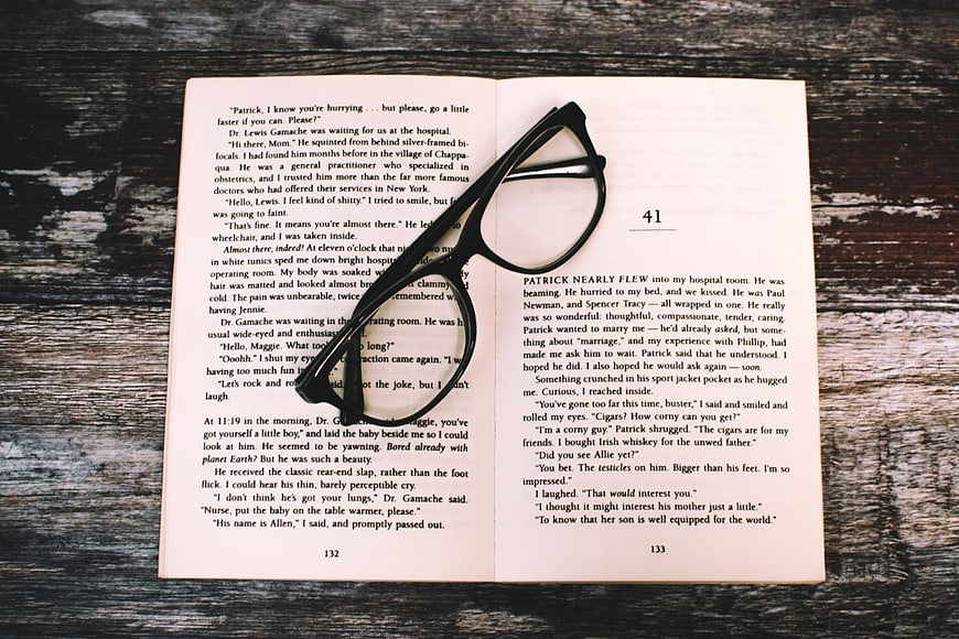 Open Book with Black Glasses on Rustic Wood