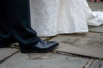 Close-up of groom's black shoe and bride's white dress hem