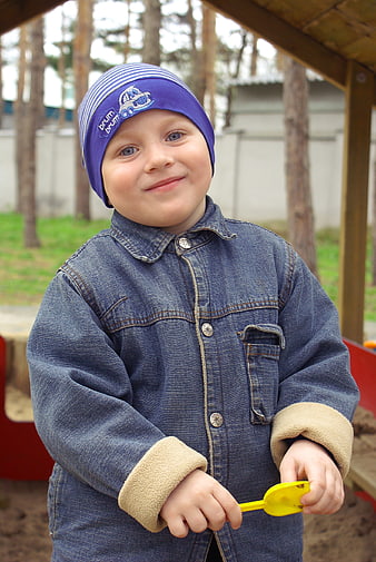 Smiling toddler boy in denim jacket playing in sandbox
