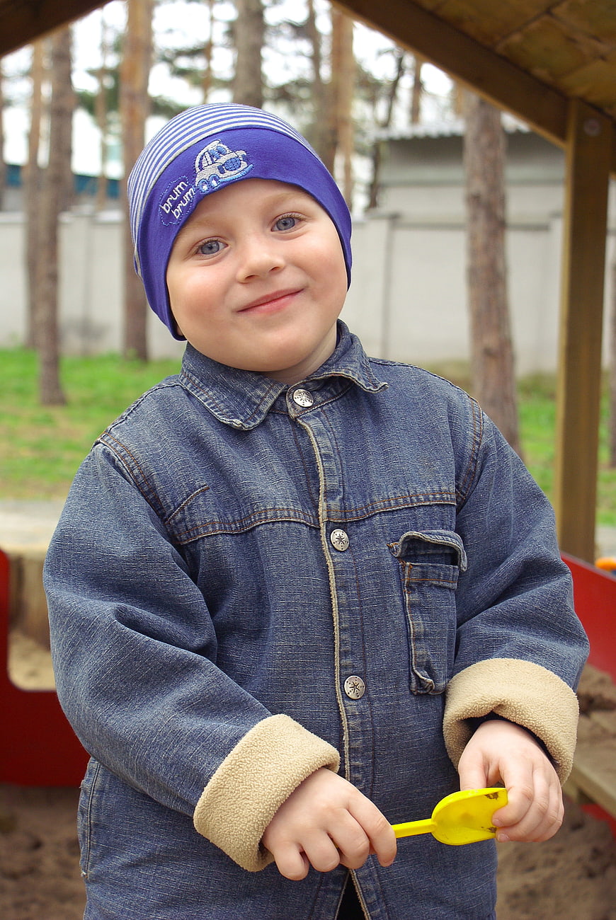 Smiling toddler boy in denim jacket playing in sandbox