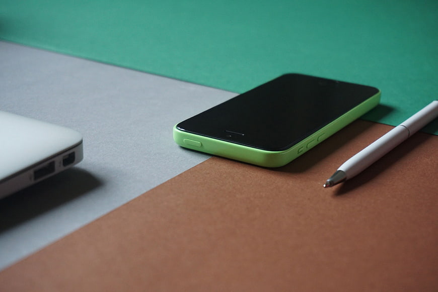 Green smartphone and pen on colorful paper background
