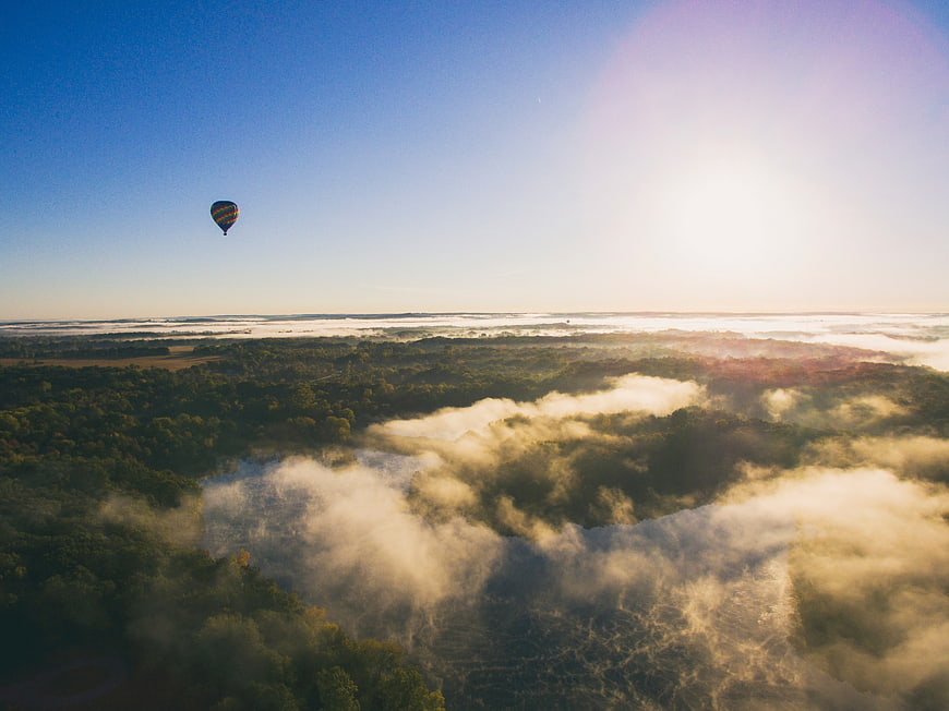 Aerial View of Hot Air Balloon Over Misty Forest at Sunrise