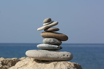 Balanced Stack of Smooth Stones on Rocky Shore by Sea