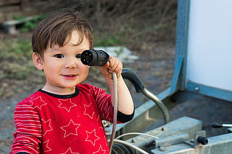 Cute young boy holding an electrical plug near his eye