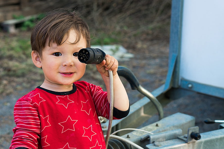 Cute young boy holding an electrical plug near his eye