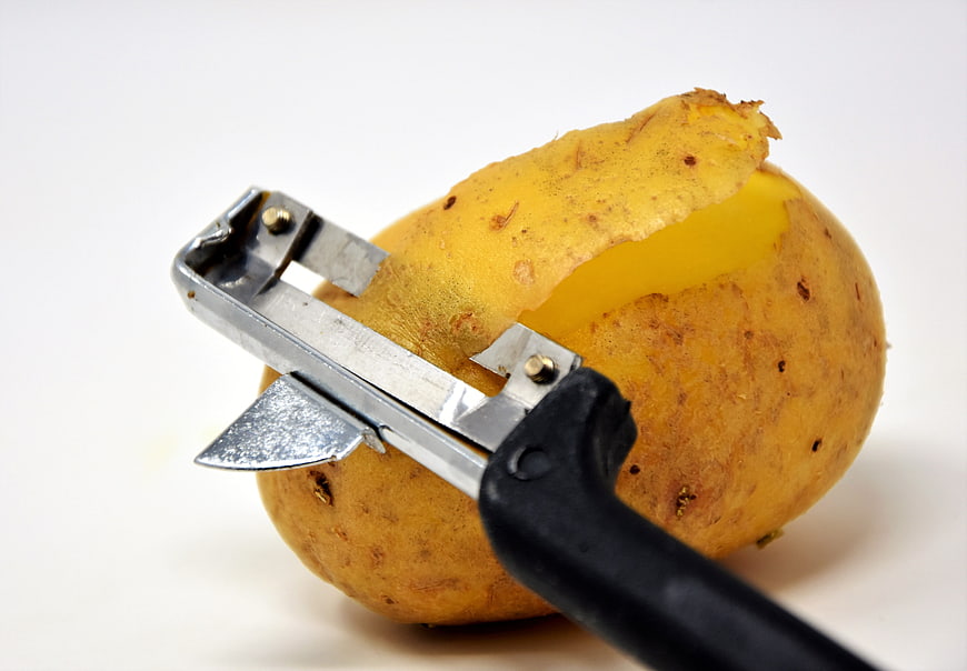 Close-up of a metal peeler removing skin from a raw potato