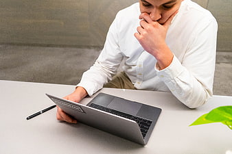 Pensive Man in White Shirt Working on Laptop at Desk