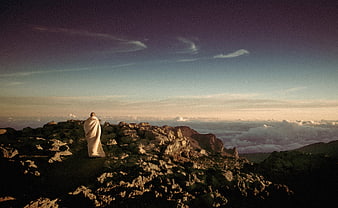 Woman wrapped in blanket on mountain peak at sunset