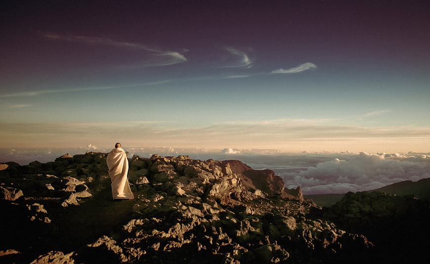 Woman wrapped in blanket on mountain peak at sunset