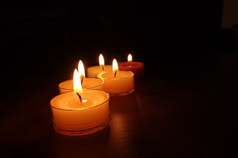 Five lit tea light candles glowing warmly on a dark wooden table