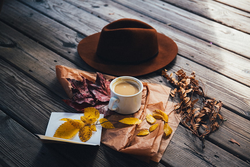 Autumn flat lay with coffee, hat, and yellow leaves on wood