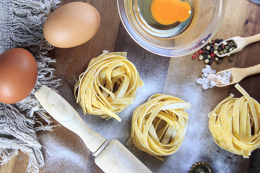 Fresh Pasta Nests with Eggs and Ingredients on Wooden Table