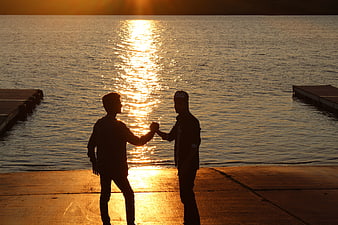 Silhouette of two friends fist bumping at sunset by the lake