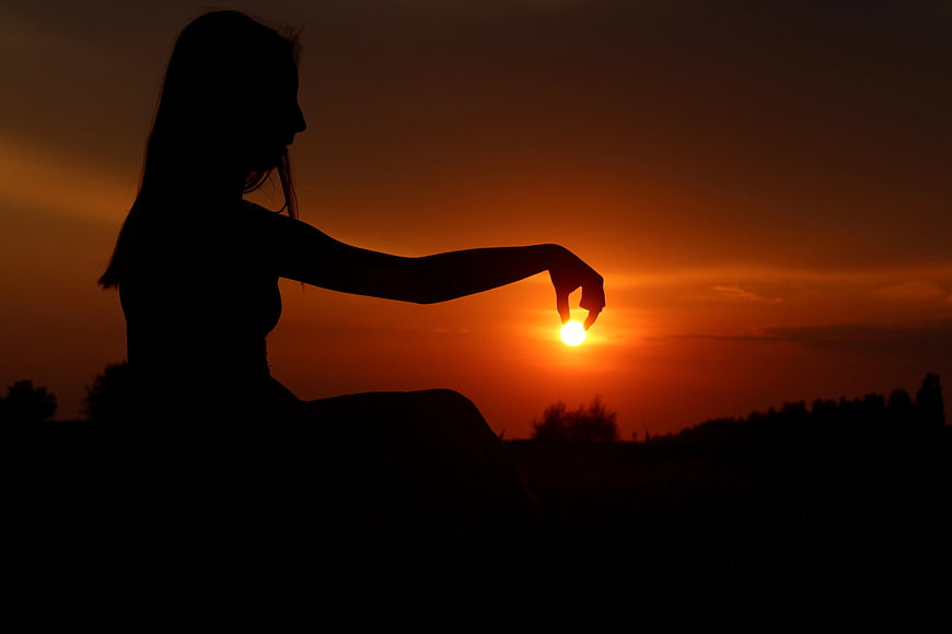 Silhouette of Woman Holding Sun at Sunset