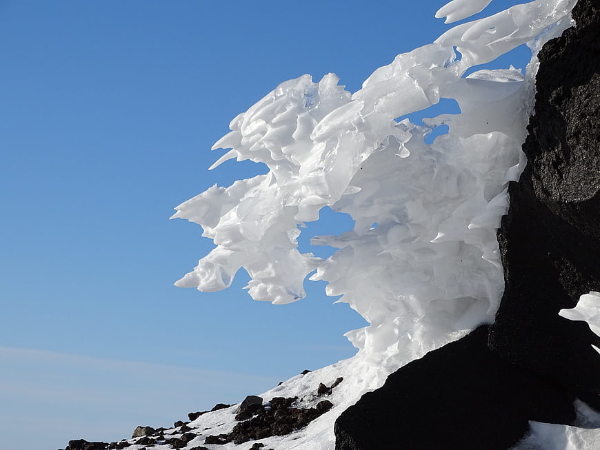 White Ice Formations on Black Volcanic Rock Against Blue Sky