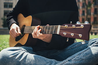 Close-up of hands playing acoustic guitar outdoors