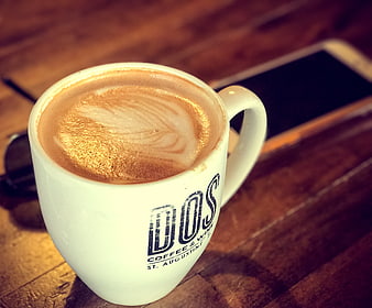 Cappuccino in white mug on wooden table with smartphone