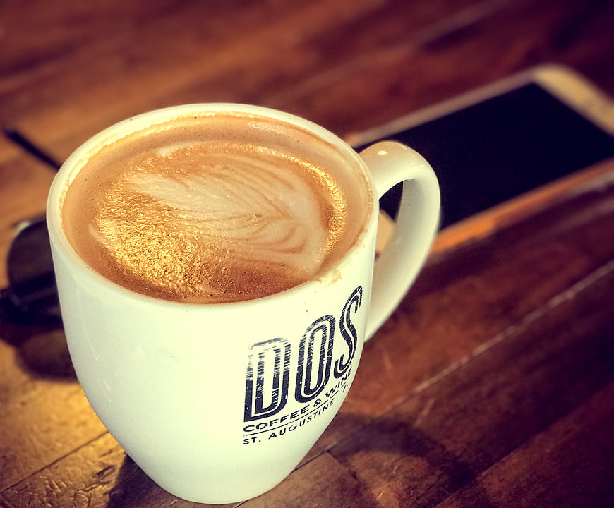 Cappuccino in white mug on wooden table with smartphone