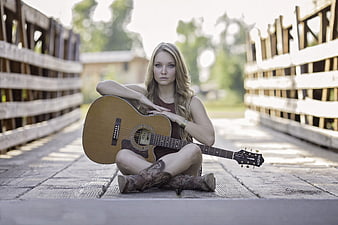 Young woman with acoustic guitar sitting on wooden bridge