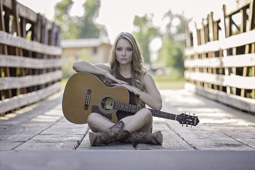 Young woman with acoustic guitar sitting on wooden bridge