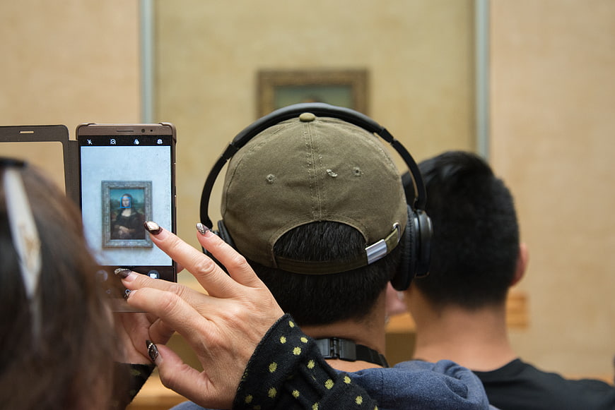 Woman photographing Mona Lisa painting with smartphone in museum