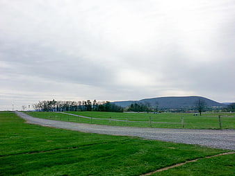 Gravel Road Winding Through Green Pasture with Distant Hills
